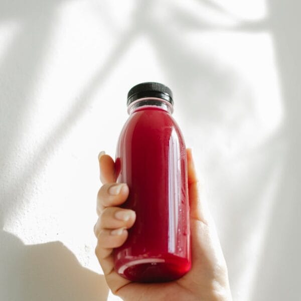 A hand holding a refreshing red juice bottle against a white background, conveying health and freshness.