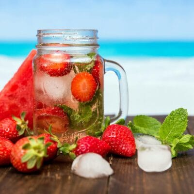 Chilled drink with strawberries, watermelon, and mint in a mason jar, perfect for summer refreshment.