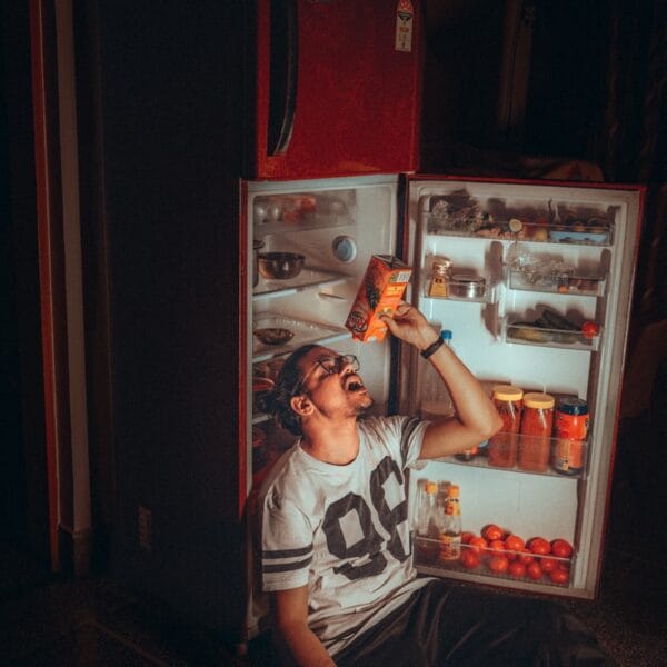 boy in white and black tank top standing beside red top mount refrigerator